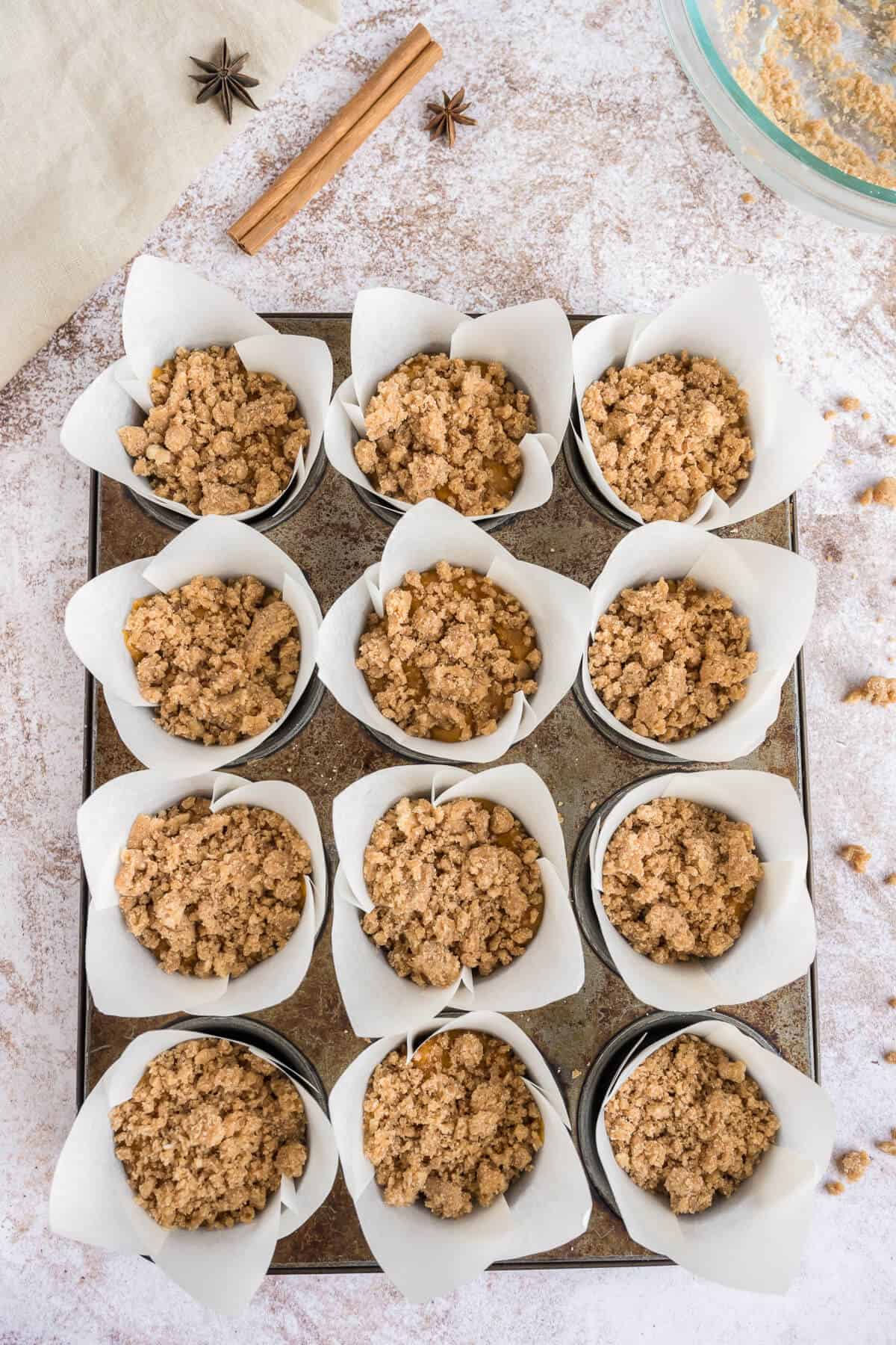 Lined muffin tin with pumpkin muffin batter poured in and topped with the raw streusel.