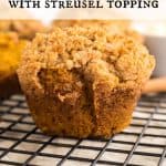 Pumpkin Muffin with Streusel topping on a. baking rack with more muffins blurred out behind it. Text overlay reads: Pumpkin Muffins with Streusel Topping.